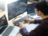 Man working with programming codes on a desktop and laptops.